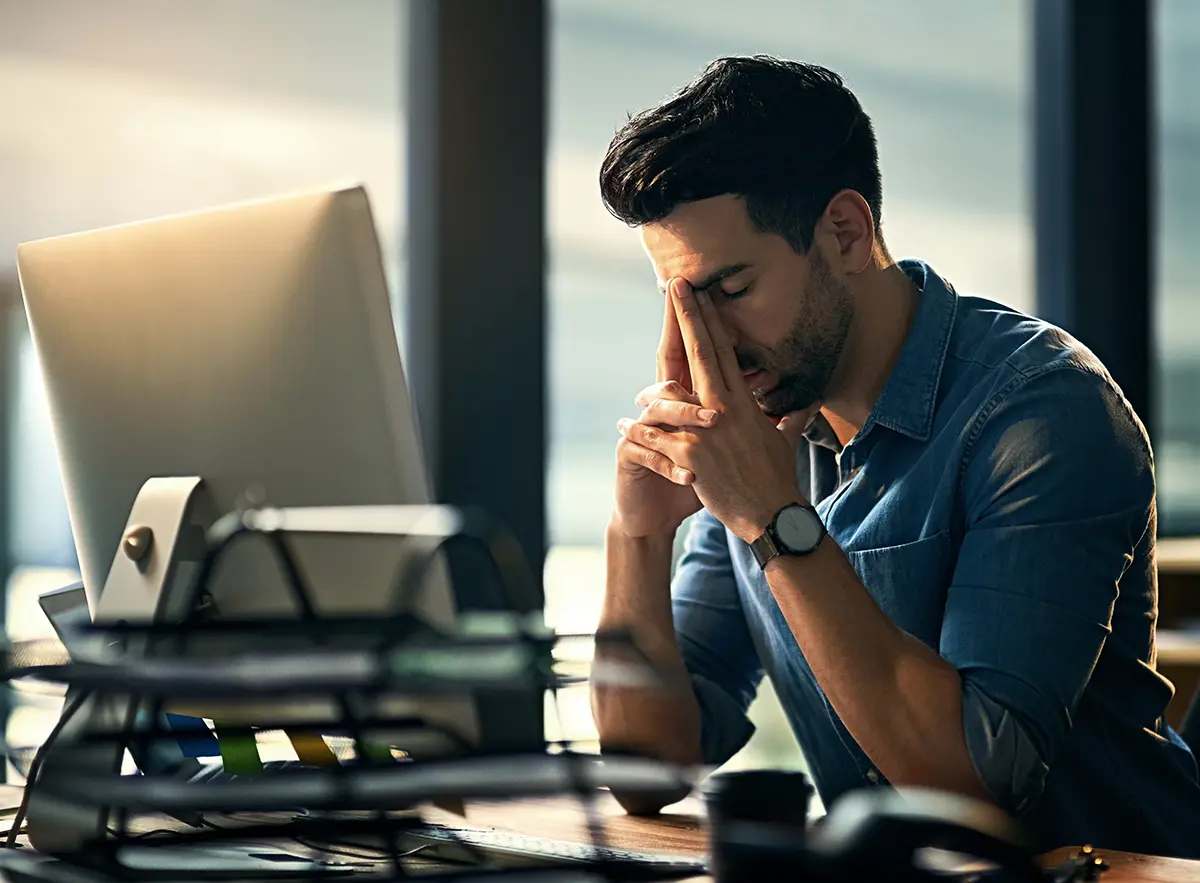 A man at his computer with his face in his hands, stressed from a data breach.