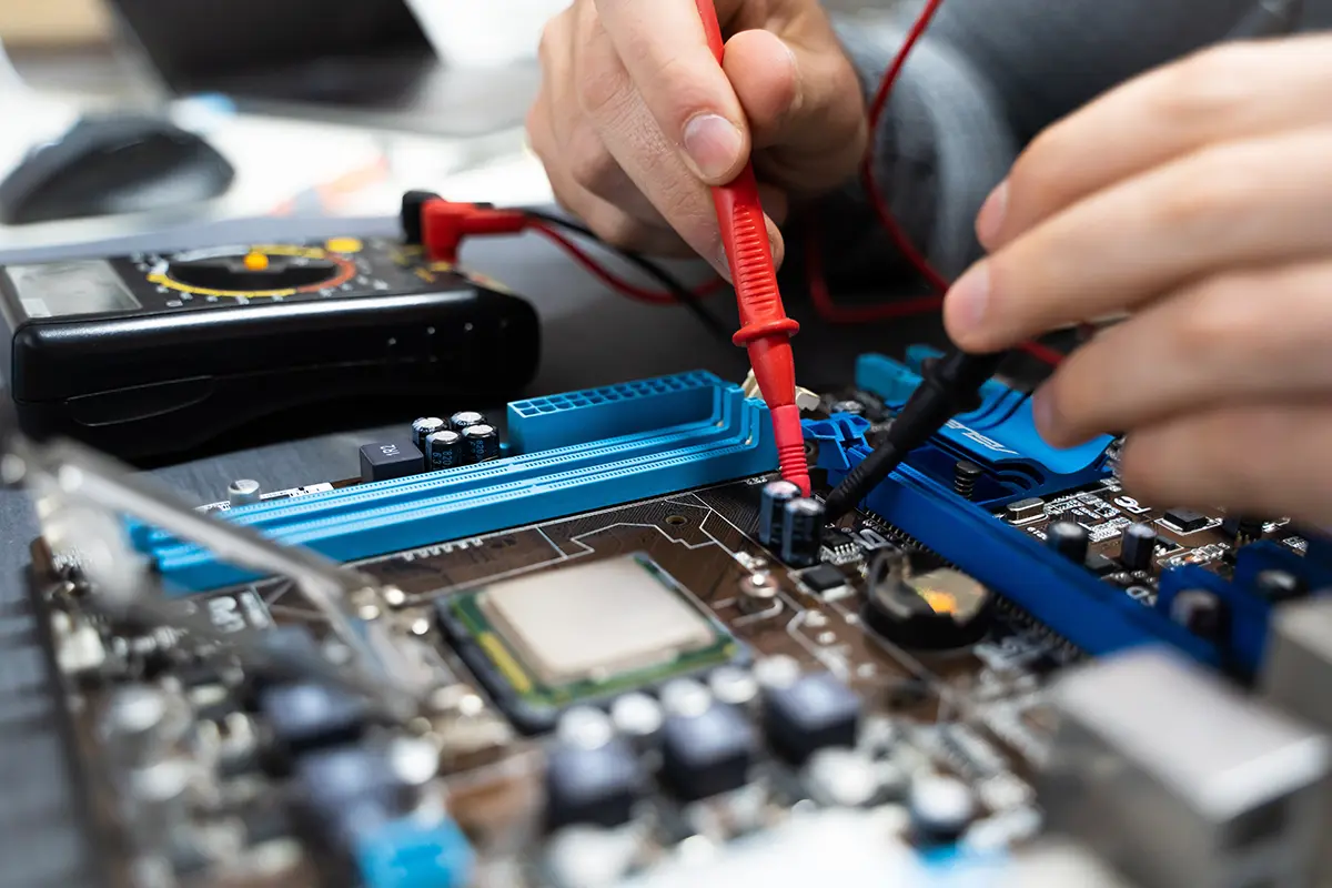An IT technician checking voltages on a motherboard with a voltmeter.