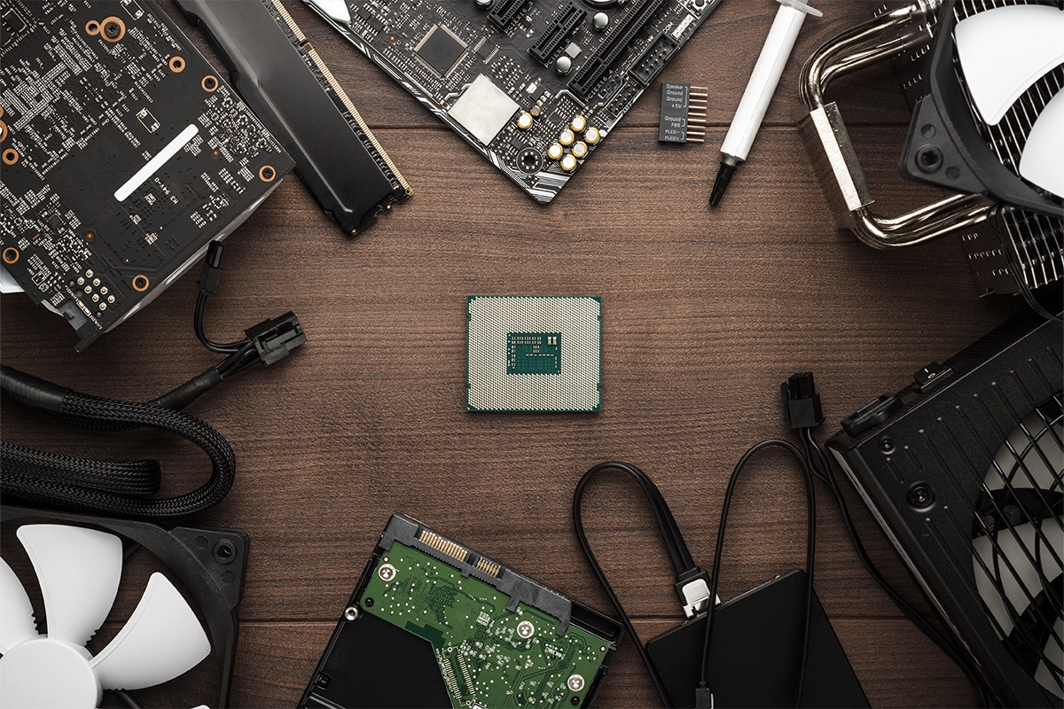 Computer processor surrounded by motherboard, graphics card, cooling fan, and other PC components on a wooden desk.