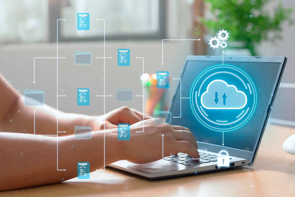 Hands typing on laptop with digital cloud backup icons representing online data storage and file synchronization.