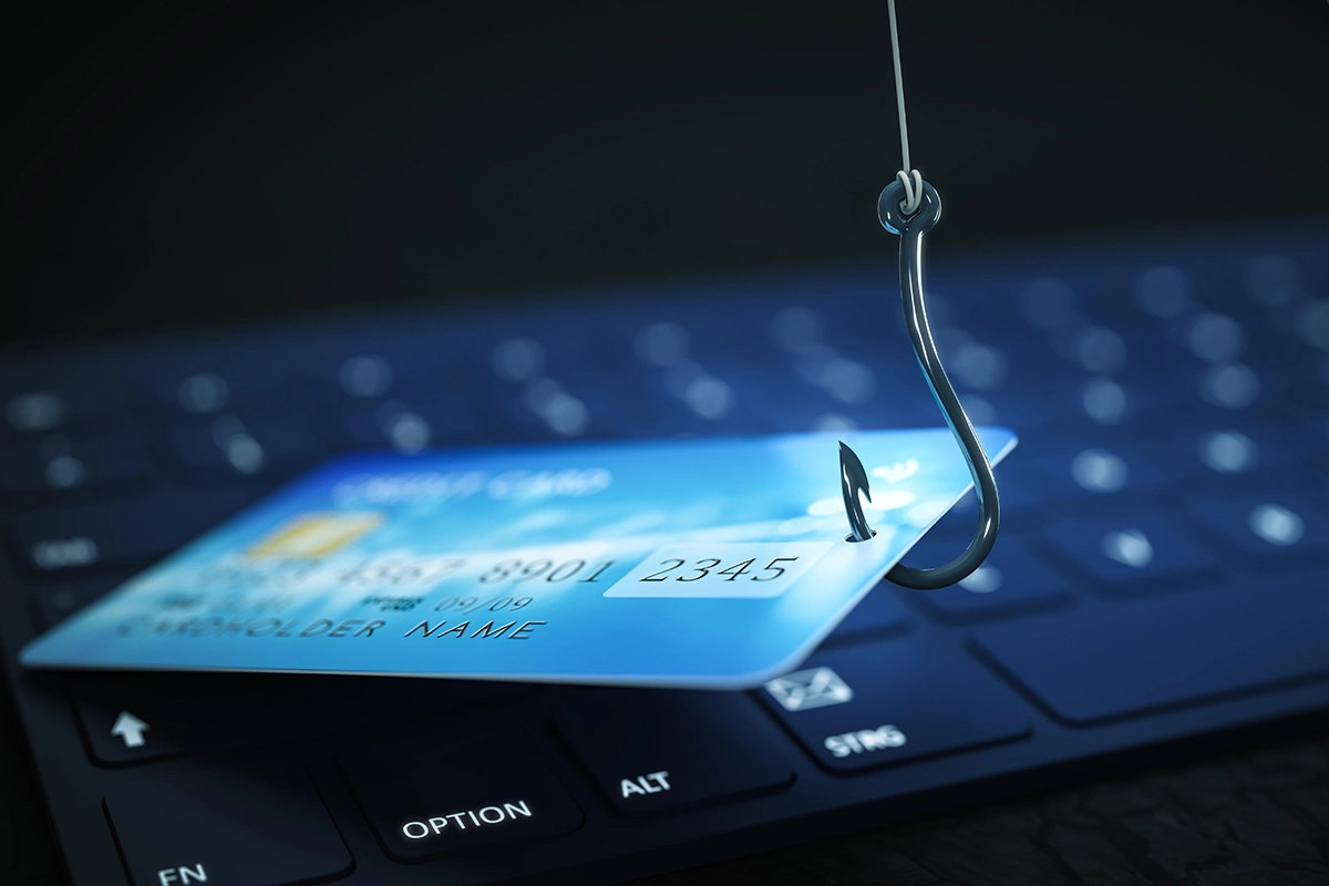 Fishing hook catching a credit card on a computer keyboard, symbolizing online phishing scams and credit card fraud.