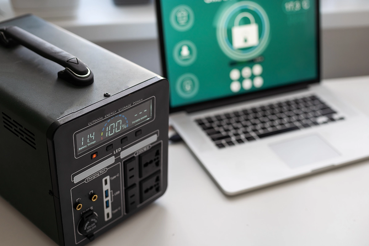 Power Station - Computer Headquarters Portable backup power station connected near laptop displaying a security lock screen, symbolizing data protection and power continuity.