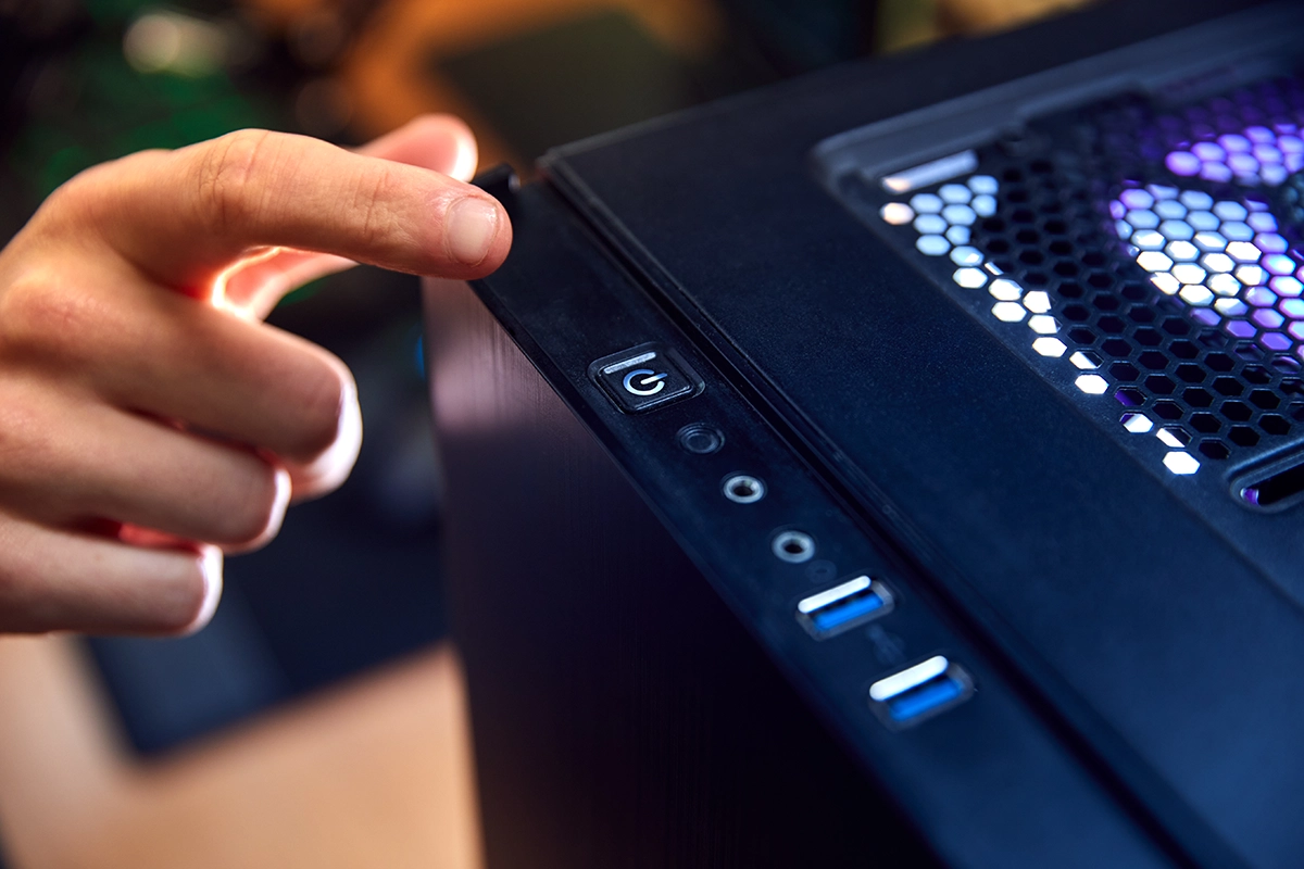 Close-up of a person pressing the power button on a desktop computer tower with glowing internal lights.