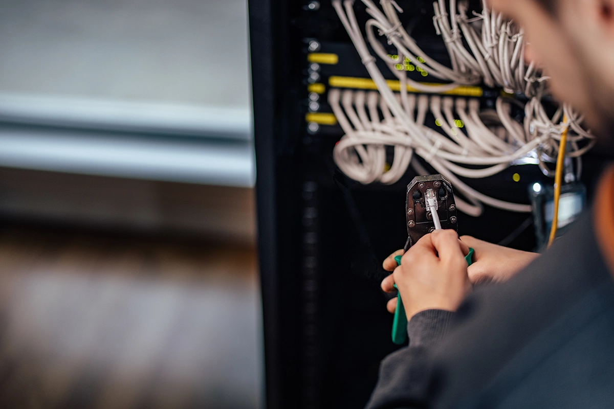 IT technician using a crimping tool to connect an Ethernet cable in a network server rack.
