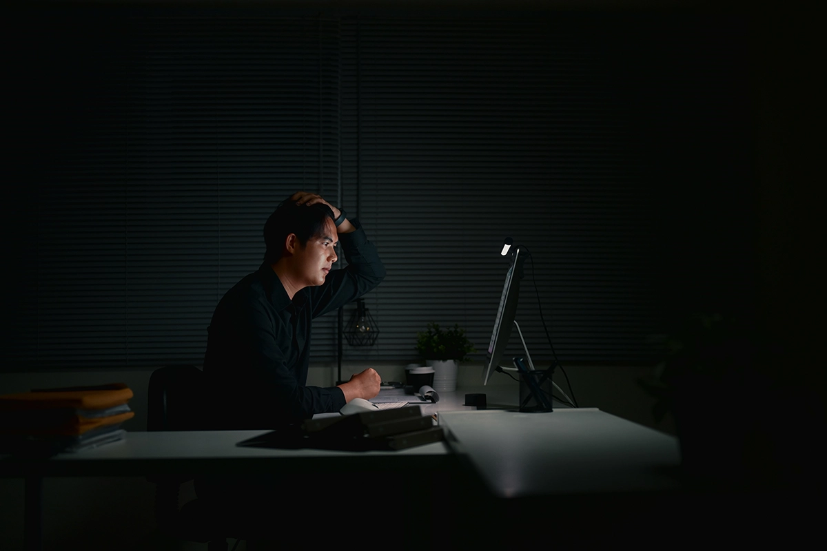 Man sitting in a dark office, frustrated while working late at night in front of a computer screen.