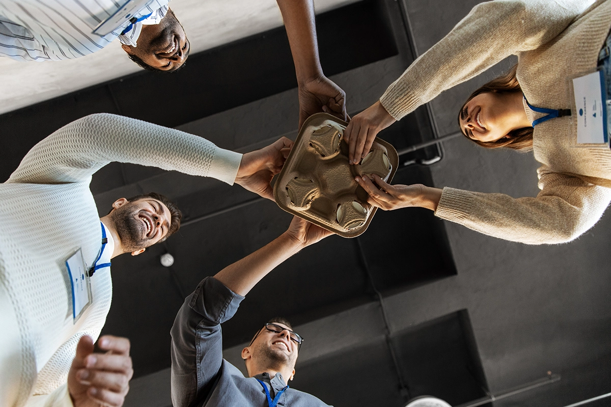 Group of coworkers smiling and holding a drink tray together, representing teamwork and office collaboration.