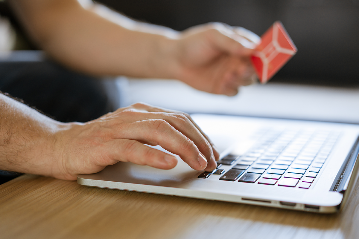 Person typing on a laptop while holding a credit card, representing online purchases or digital payment entry.