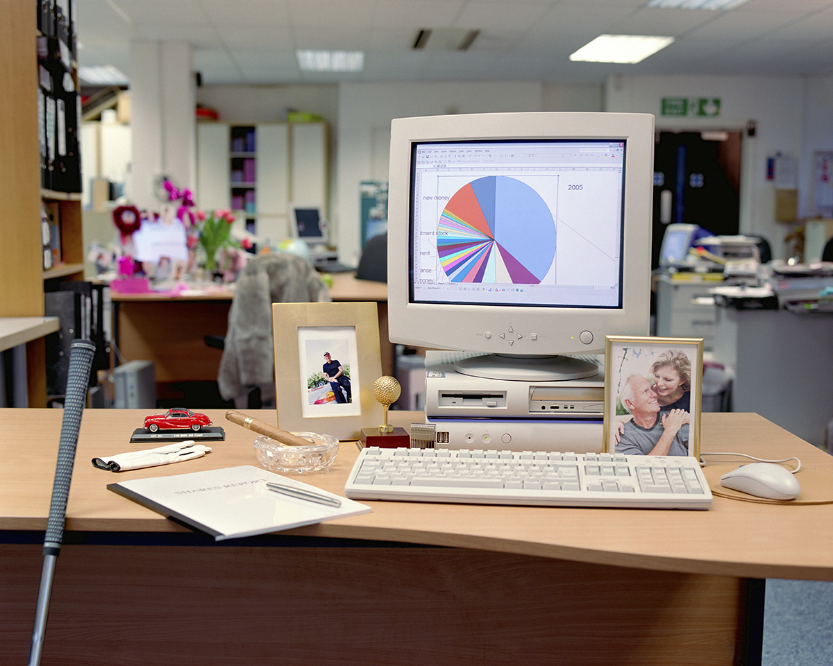 Vintage office desk setup with an older desktop computer displaying a pie chart, framed photos, and personal desk items in a workplace environment.