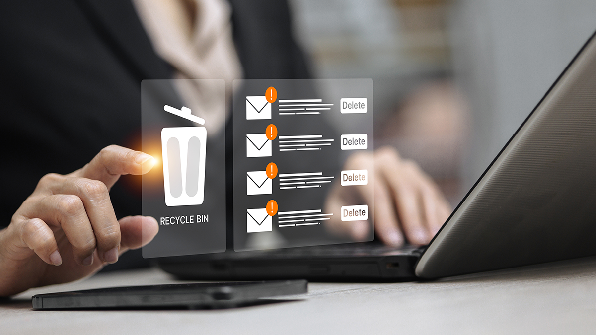 Person using a laptop interface to delete emails with a recycle bin icon and warning indicators, representing inbox cleanup and email management.