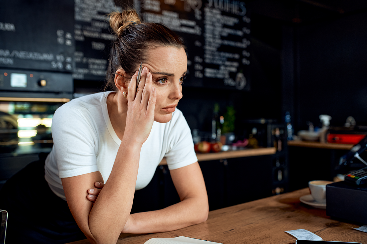 Stressed business owner leaning on a counter with a concerned expression, representing operational stress and technology challenges.