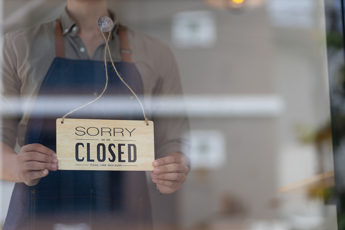 Person holding a sorry we are closed sign in a shop window, representing temporary business closure or service interruption.