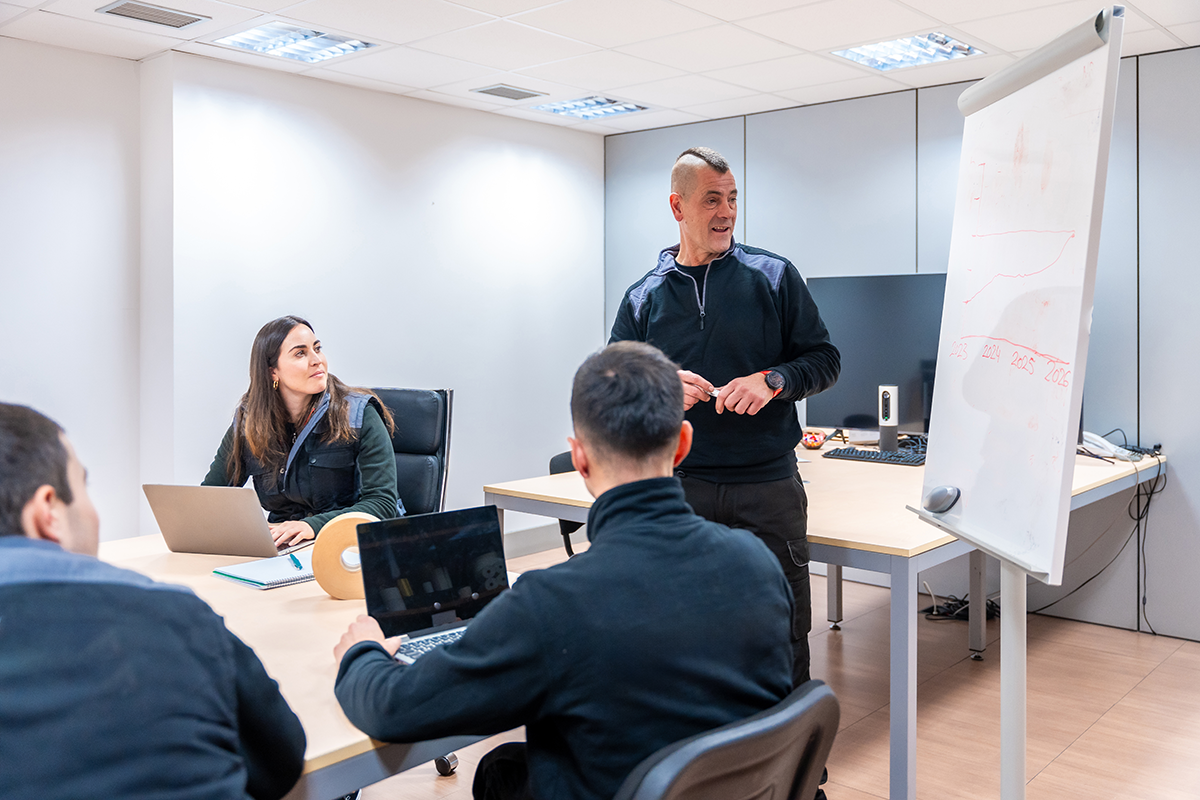Team meeting in a modern office with a manager presenting information on a whiteboard, representing employee training and business collaboration.