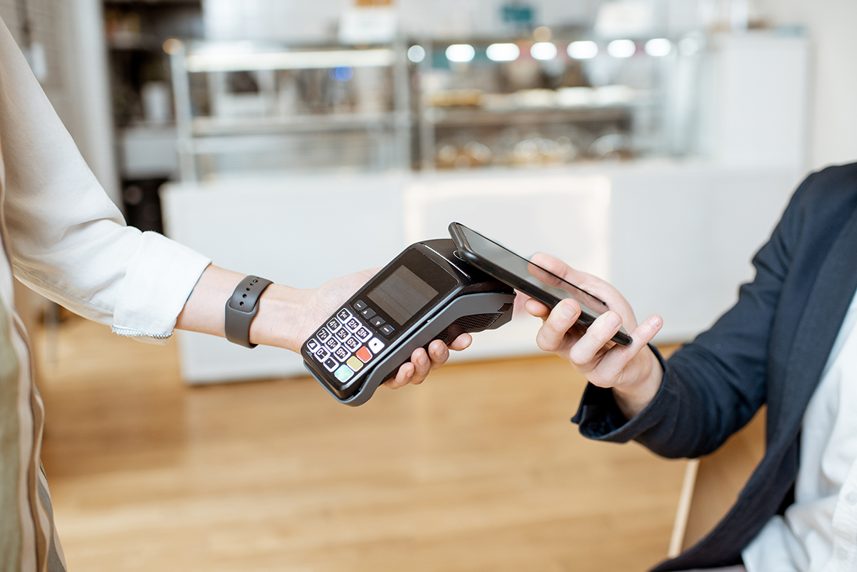 Customer making contactless payment with smartphone and card terminal at checkout
