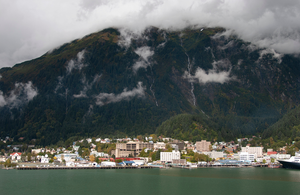 Coastal town and harbor at the base of forested mountains in Southeast Alaska under low clouds