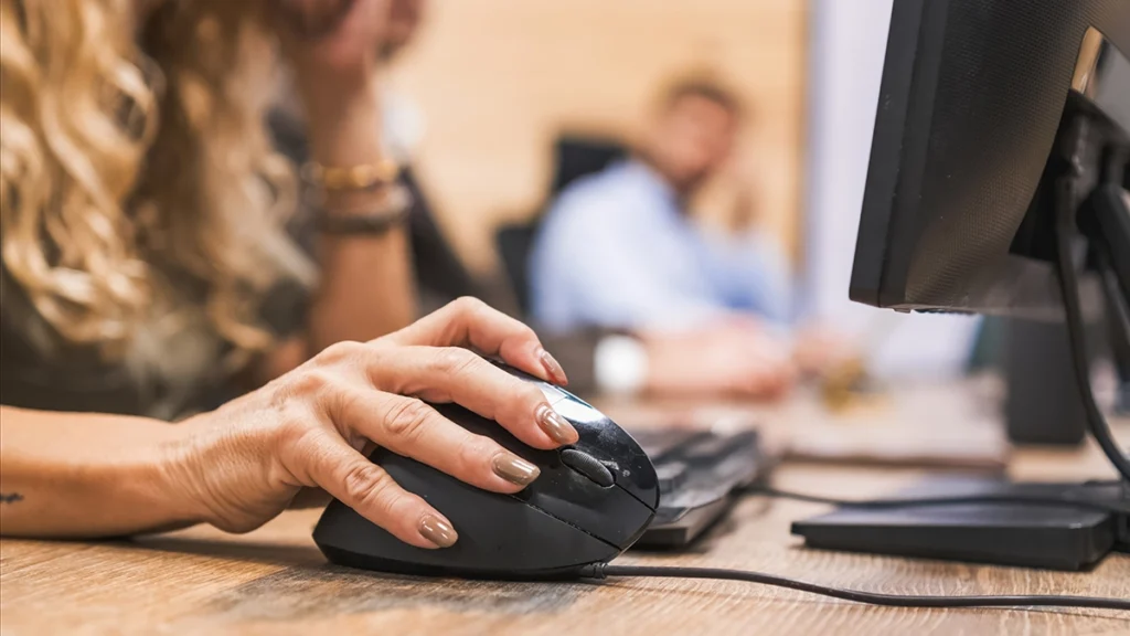 Close-up of person using a computer mouse at a desk in an office workspace