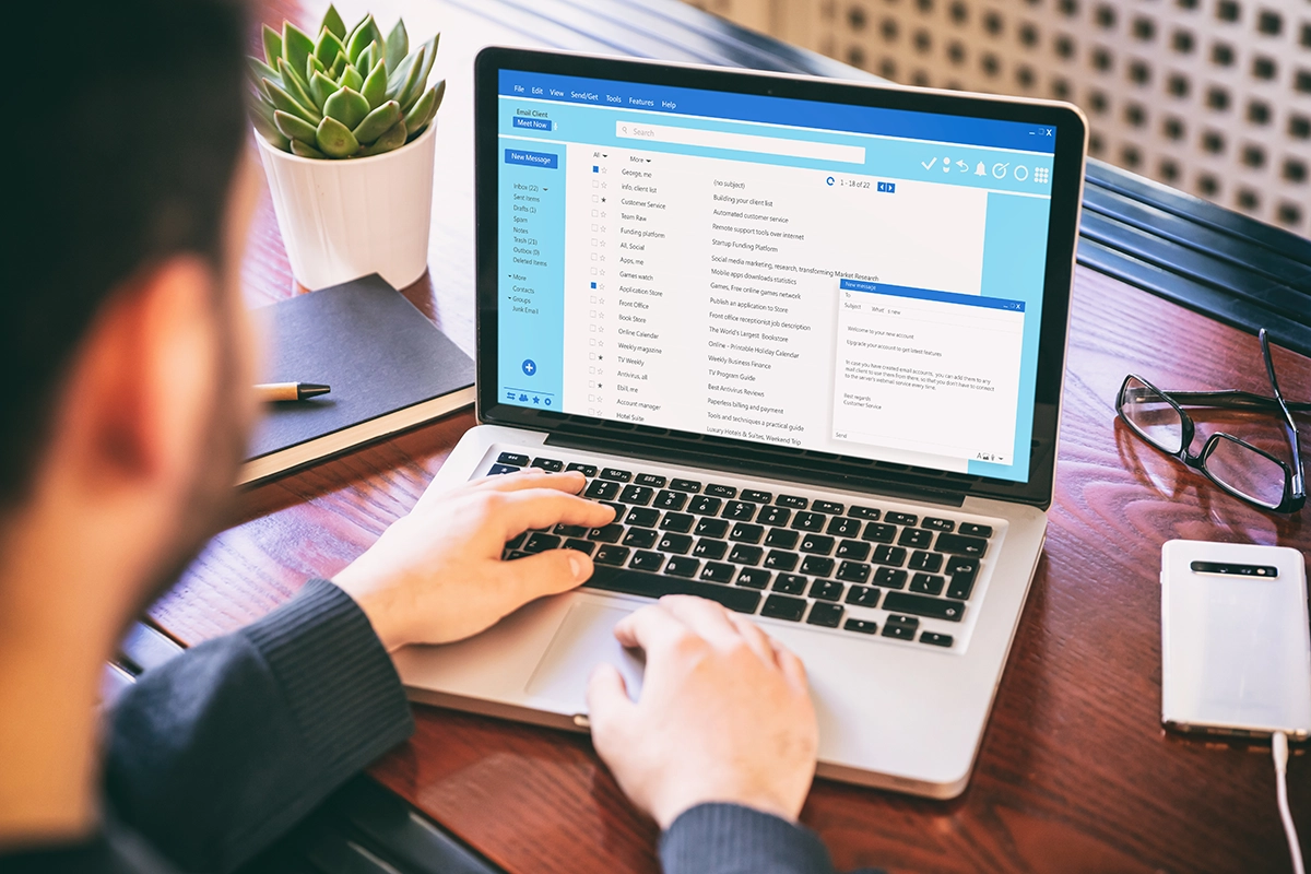 Man using laptop to check emails at desk with smartphone and office accessories